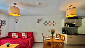 A compact living space with a red sofa, wooden dining table, and a kitchenette. - T2 vue Montagne, Accès Direct aux Pistes, Avec Piscine (Vars)