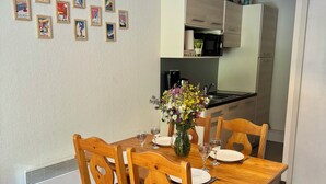 A dining area with a wooden table set for four, surrounded by chairs with heart-shaped cutouts. A vase with flowers is on the table, and a wall-mounted light fixture is above. - T2 vue Montagne, Accès Direct aux Pistes, Avec Piscine (Vars)