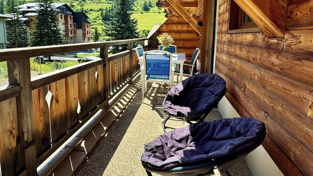 A wooden balcony with two covered chairs, a table, and a view of a green mountain landscape. - T2 vue Montagne, Accès Direct aux Pistes, Avec Piscine (Vars)