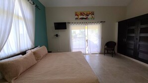 A bedroom with a bed, a chair, a TV, and a sliding door leading to a balcony. - Villa Hermosa Spacious Close Town And Sosua Beach (Sosúa)