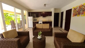 A living room with wicker furniture, a small round table with a plant, and a kitchen in the background. - Villa Hermosa Spacious Close Town And Sosua Beach (Sosúa)