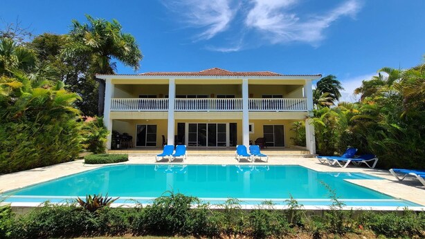 A two-story building with a swimming pool, blue lounge chairs, and lush greenery. - Villa Hermosa Spacious Close Town And Sosua Beach (Sosúa)