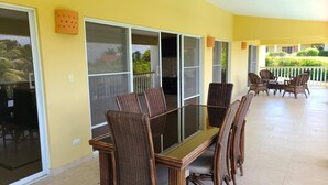 A covered outdoor area with a dining table and chairs, large sliding glass doors, and a view of greenery outside. - Villa Hermosa Spacious Close Town And Sosua Beach (Sosúa)