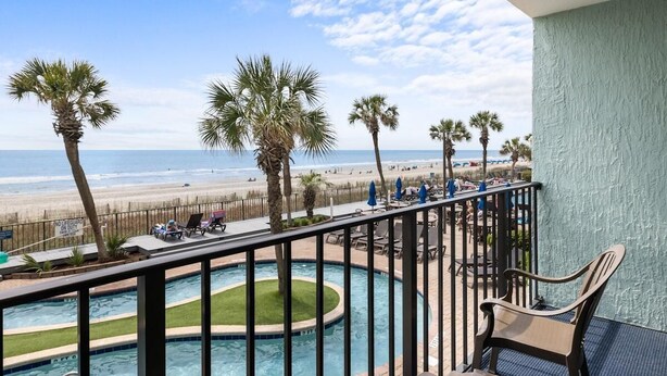 A balcony with a view of a beach and a swimming pool. - Seaside Adventures-Oceanfront Room 3rd Floor (Myrtle Beach)