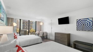 Ein Hotelzimmer mit zwei Betten, einem Schreibtisch, einem Stuhl, einem Fernseher und einem Balkon mit Blick.
