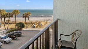 Ein Balkon mit Blick auf den Strand, parkende Autos und einem Stuhl.