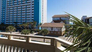 A hotel with a modern design, featuring a prominent blue and white facade, a traditional building with a brown roof, and a view of the surrounding area including palm trees and a clear sky. - Modern Coastal Retreat Two Bdrm Condo on Low Floor (Myrtle Beach)