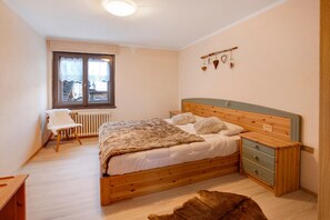 Ein Schlafzimmer mit einem hölzernen Bett, einem Sessel, einem Heizkörper und einem Fenster mit Spitzenvorhängen.