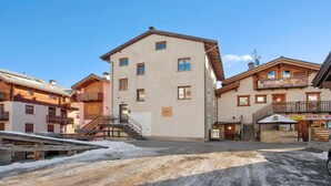 A building with a staircase leading to a second floor, a sign for a bar, and a snow-covered ground. - Apartment 'Lovin Winter' with Mountain View, Private Balcony and Wi-Fi (Livigno)