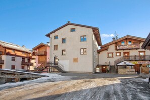 Un edificio de varios pisos con una escalera que conduce a la entrada, un letrero y el suelo cubierto de nieve.