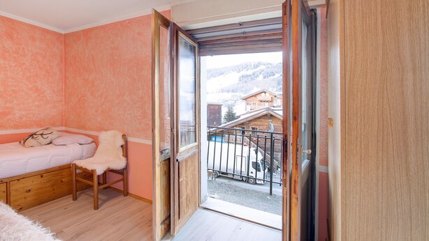 A bedroom with a bed, a chair, a window, and a balcony. - Apartment 'Lovin Winter' with Mountain View, Private Balcony and Wi-Fi (Livigno)