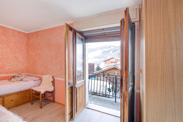 Un dormitorio con cama, una silla, una ventana y un balcón.