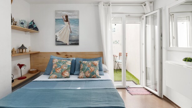 Une chambre à coucher avec un lit, des oreillers, un tableau, une fenêtre et une porte donnant sur un balcon.