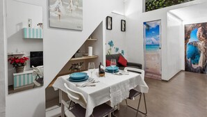 Un coin repas avec une table dressée pour deux personnes, un mur blanc orné d’œuvres d’art, un escalier et une vue sur l’extérieur.