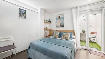 Een slaapkamer met een bed, een stoel, een bureau, een raam en een deur die leidt naar een balkon.