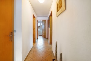 A hallway with a tiled floor, wooden doors, and a framed picture on the wall.