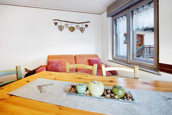 A dining area with a wooden table, chairs, a bench, and a window with curtains.