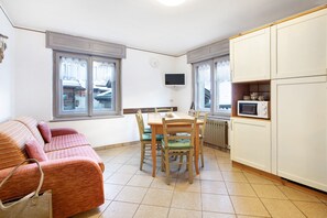 A compact kitchen with a dining table, chairs, a TV, and a sofa.