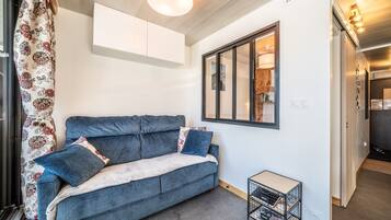 A modern living room with a sofa, a small side table, a window with a view, and a door leading to another room.