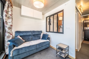 Un salón moderno con un sofá, una mesita auxiliar, una ventana con vistas y una puerta que da a otra habitación.