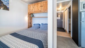 A bedroom with a bed, wooden cabinets, a refrigerator, and a hallway leading to a bathroom. - Apartment 'Les Mouflons 1500' with Mountain View, Balcony and Wi-Fi (Taninges)