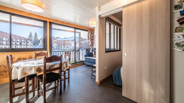 A dining area with a table and chairs, a sofa, a small side table, and a view of buildings outside. - Apartment 'Les Mouflons 1500' with Mountain View, Balcony and Wi-Fi (Taninges)
