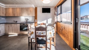 A modern kitchen with wooden cabinets, a dining table with chairs, a built-in oven, and a TV mounted on the wall. - Apartment 'Les Mouflons 1500' with Mountain View, Balcony and Wi-Fi (Taninges)