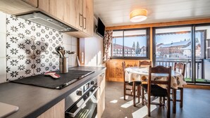 A modern kitchen with wooden cabinets, a black countertop, and a dining area with a table and chairs. - Apartment 'Les Mouflons 1500' with Mountain View, Balcony and Wi-Fi (Taninges)