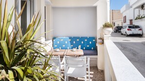 Un balcon avec une chaise blanche, une petite table sur laquelle se trouve une tasse, et un coussin bleu.
