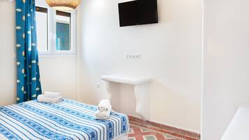 A bedroom with a bed, a window with curtains, a mounted TV, a white sink, and a patterned floor.