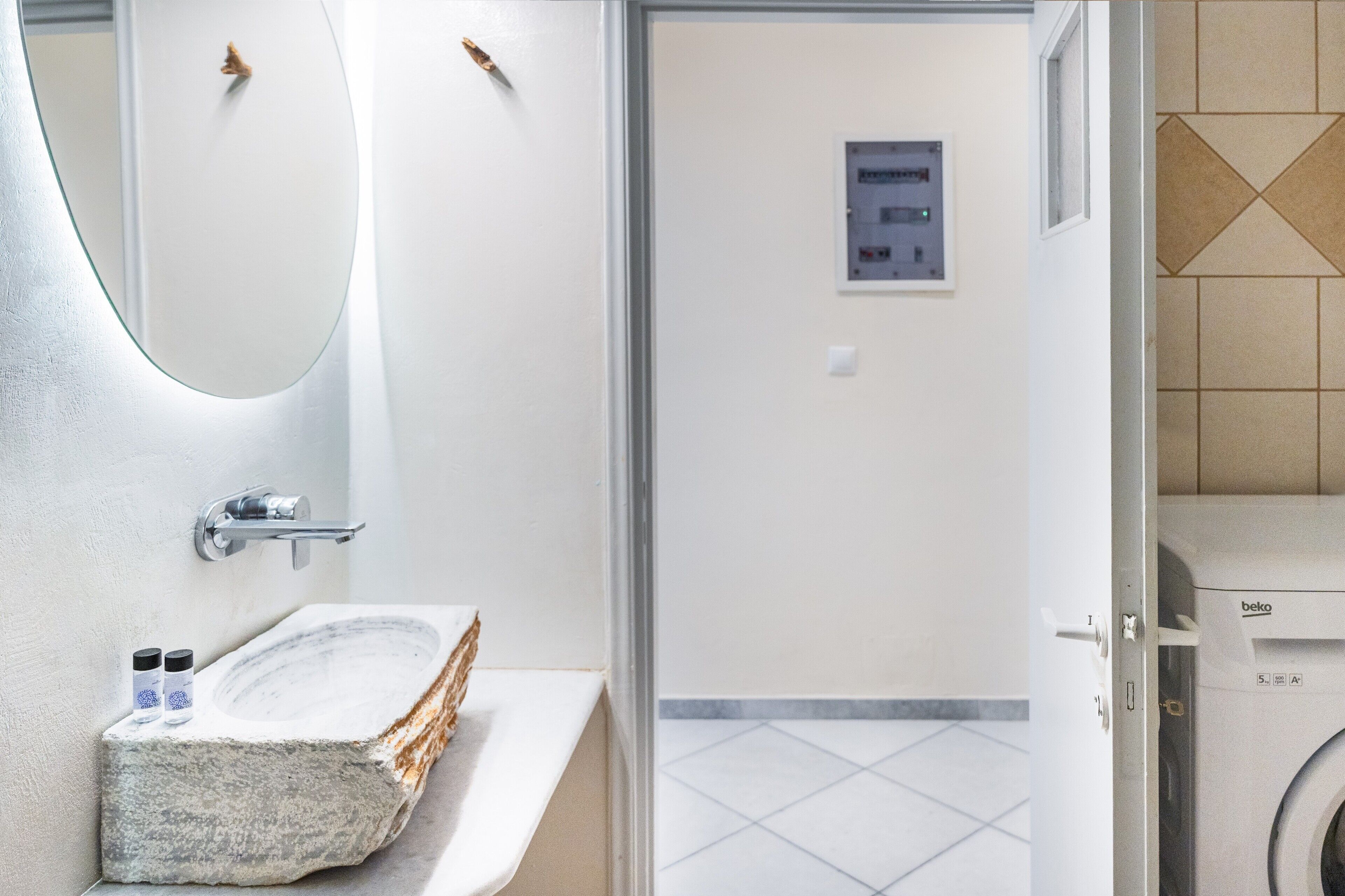 A bathroom with a stone sink, a mirror, a wall-mounted light, and a washing machine.