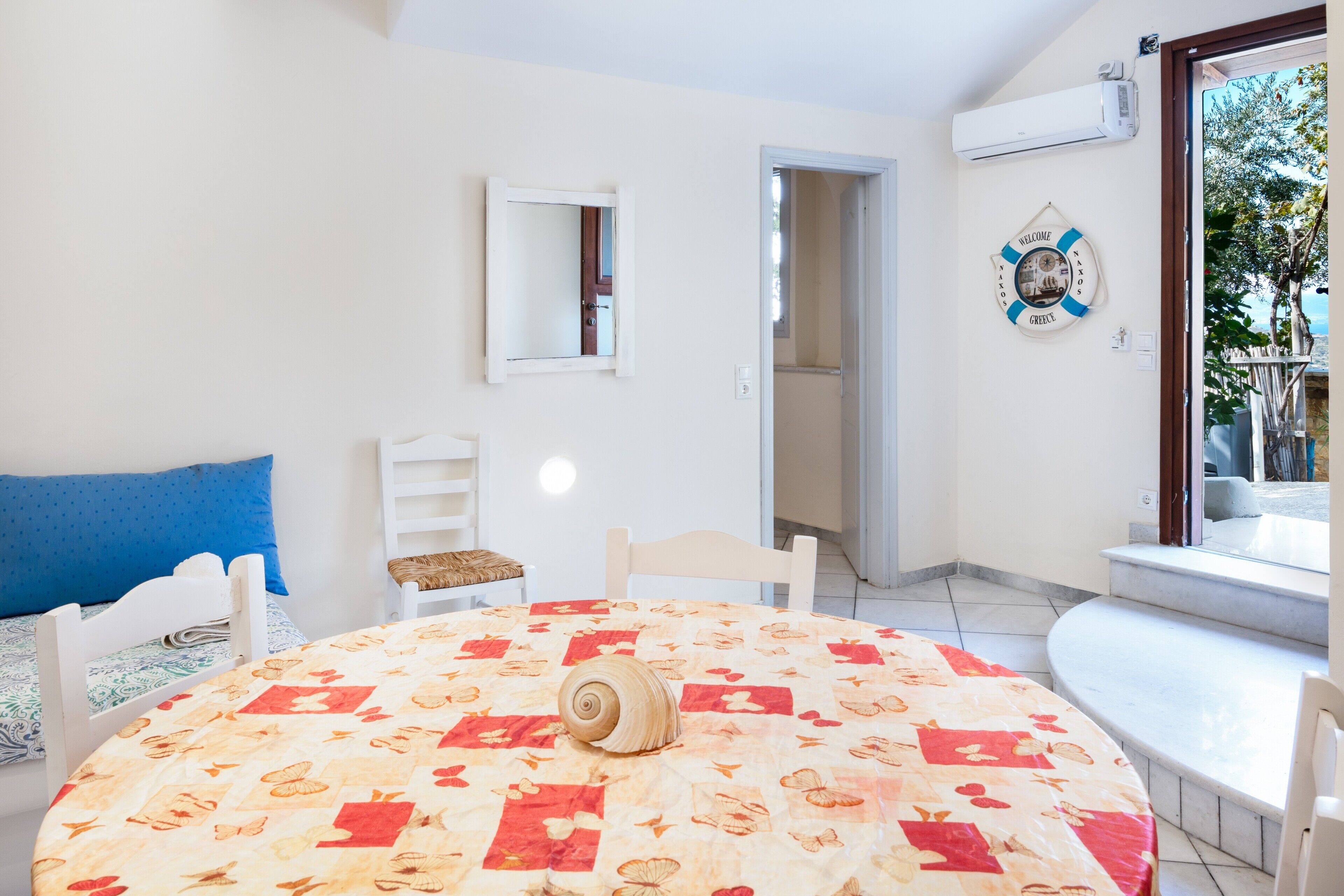 A room with a round table, a bed with a blue pillow, a chair, a mirror, and a welcome sign.