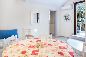 A room with a round table, a bed with a blue pillow, a chair, a mirror, and a welcome sign.