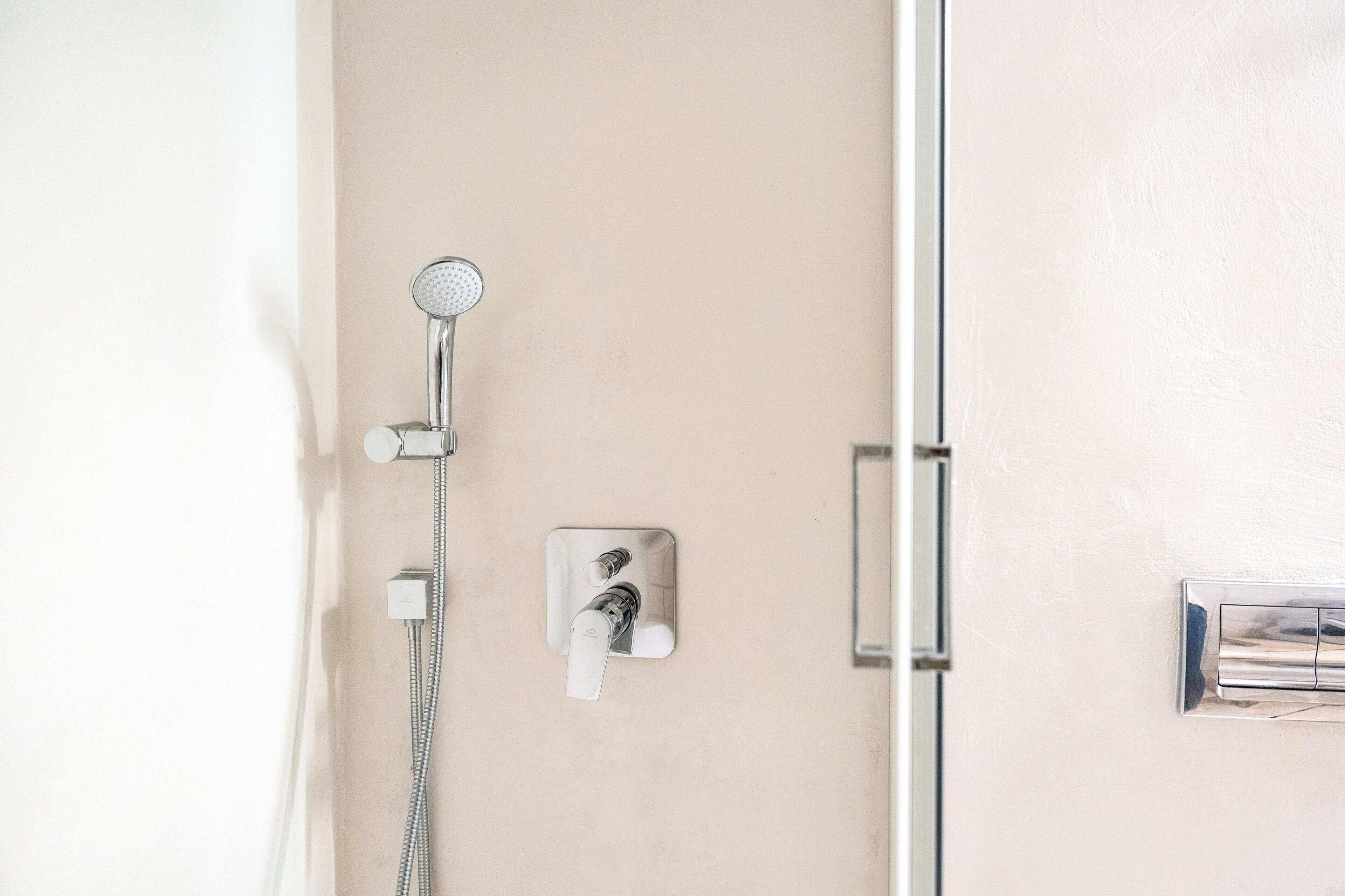 Ducha con cabezal de ducha de mano y panel de control en la pared.