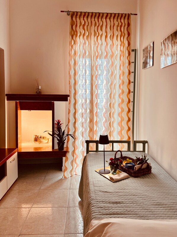 Un dormitorio con cama, mesita de noche, lámpara y ventana con cortinas.