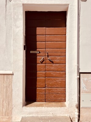 Una puerta de madera marrón con un picaporte de metal y cerradura, en una pared blanca con un pequeño escalón que lleva a ella.