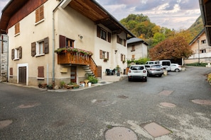 A building with a stone facade, wooden shutters, and a balcony with potted plants.
