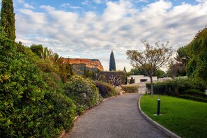 A gravel path leading through a landscaped area with dense shrubbery and a view of a building with a stone facade.