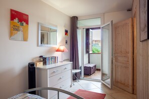 Une chambre d’hôtel avec un lit, un bureau avec une lampe, une armoire, une petite table avec une horloge et une fenêtre donnant sur l’extérieur.