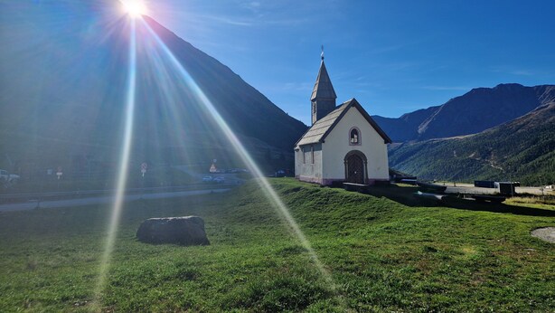 En liten kyrka med ett torn, omgiven av gröna kullar och en klar himmel.