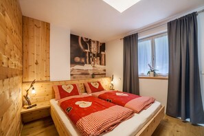 Une pièce avec un mur en bois, un lit recouvert d’une couette à carreaux rouges et blancs, une table de chevet avec une lampe, une fenêtre avec des rideaux et un tableau accroché au mur.