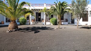 Un edificio con fachada blanca, un balcón rojo y un patio empedrado con palmeras.
