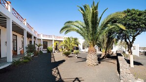Un patio con palmeras, un muro de piedra y un corredor cubierto con barandillas rojas.