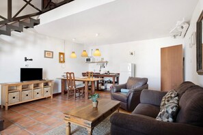 A living room with a sofa, TV, wooden table, and chairs. There is a kitchen area with a dining table and chairs. - Country House 'Finca Emblemática - Nº2 Chibusque' with Mountain Views, Pool and Wi-Fi (La Vegueta)