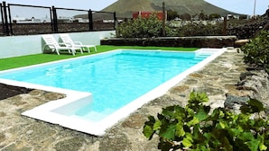 Et rektangulært swimmingpool med en hvid kant, omgivet af en stenkant, og et afspærret område med hvide liggestole.