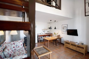 Un salon moderne avec un canapé, une table à manger en bois, un téléviseur et une cuisine en arrière-plan.