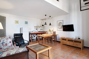 Un salon comprenant un canapé, une table à manger, des chaises, un téléviseur et un coin cuisine.