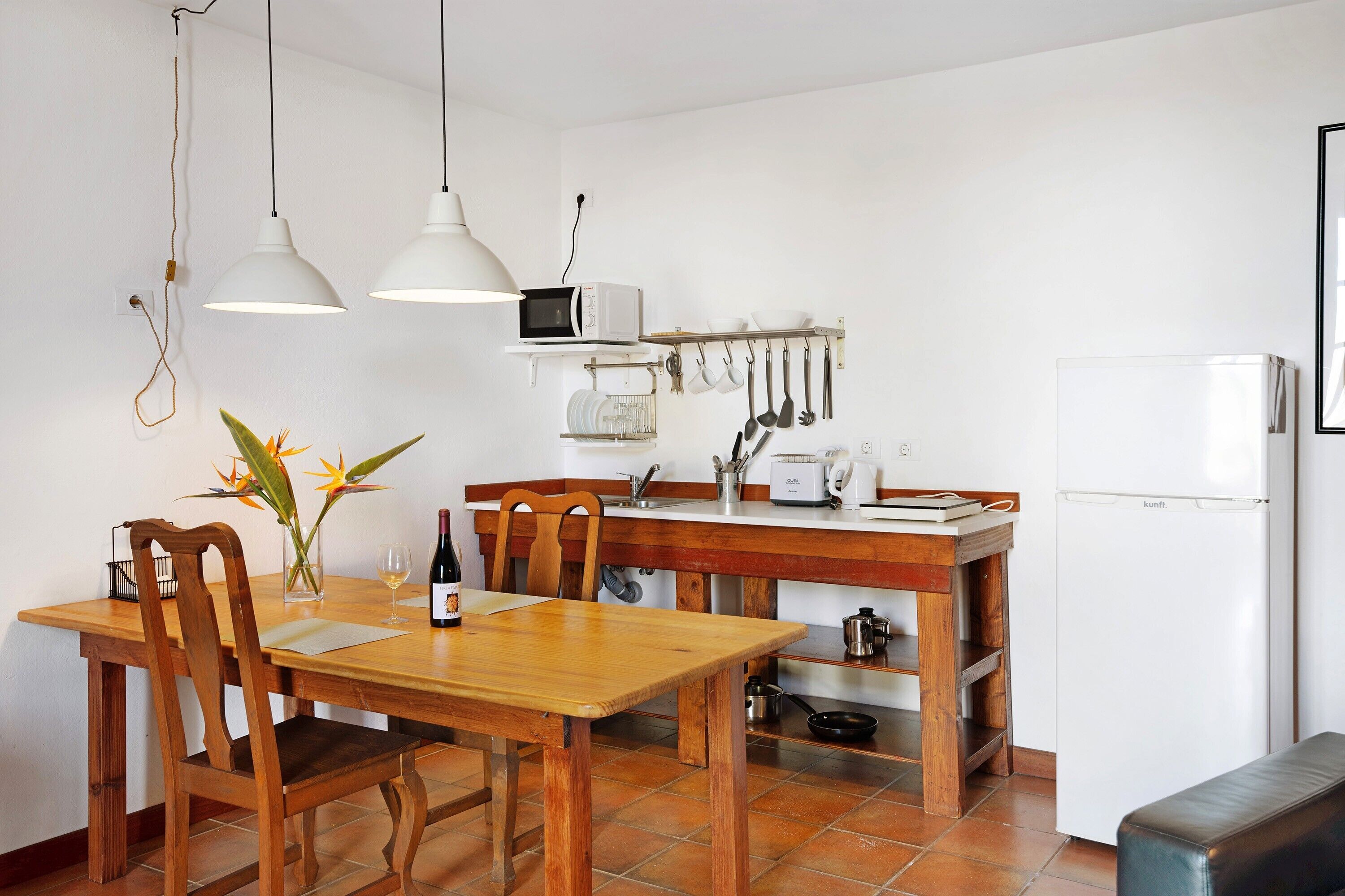 A kitchen with a wooden table, chairs, a microwave, and hanging utensils.