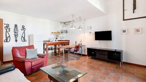 Un soggiorno con un divano in pelle rossa, un tavolino in vetro, una zona pranzo con tavolo e sedie in legno, una TV montata a parete e un angolo cottura con forno a microonde e tostapane.