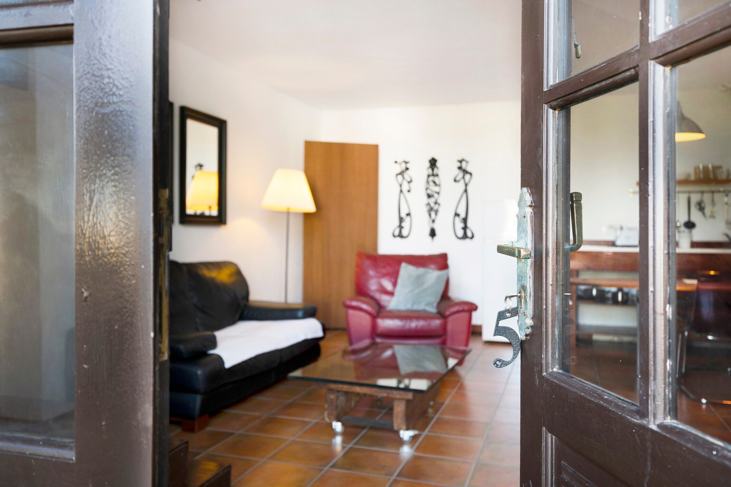 A room with a glass coffee table, a red leather sofa, a lamp, and wall art.